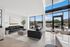 Modern living room with sleek black sofas, floor-to-ceiling windows, and a spacious outdoor patio with lush greenery.
