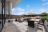 Luxurious outdoor terrace featuring a modern dining area, cozy seating with plush cushions, and a built-in BBQ grill, perfect for entertaining under a sunny sky.