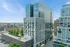 Modern high-rise building with sleek glass facade, surrounded by lush greenery, offering stunning city views on a sunny day.