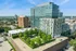 Modern urban apartment complex with lush rooftop garden, surrounded by vibrant cityscape and blue skies.