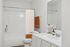 Elegant bathroom with clean white fixtures, stylish orange accents, and a large mirror enhancing natural brightness.