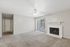 Bright living room with plush carpet, large window, and elegant fireplace under a modern ceiling fan.