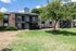 Charming apartment exterior with brick facade, surrounded by lush greenery and a sunny blue sky.