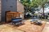 Charming outdoor area with blue picnic tables and a barbecue setup, shaded by trees next to a stylish apartment building and inviting pool area.