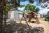 Inviting apartment playground with swings and slide, surrounded by lush trees and modern brick buildings, creating a perfect family-friendly environment.