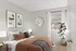Cozy bedroom with stylish decor, featuring framed art, plush pillows, and a vibrant potted plant under soft natural light.