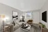 Contemporary living room with a chic beige sofa, stylish brown armchair, modern artwork, and a sleek black coffee table, complemented by natural light and tasteful decor.