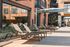 Modern apartment courtyard with sleek lounge chairs, glass facade, and stylish brick architecture for a relaxing urban retreat.