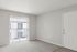 Bright and inviting apartment space featuring plush carpeting, large sliding doors with vertical blinds, and a sleek entryway.