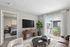 Elegant living room with contemporary decor, featuring a plush sofa, textured coffee tables, and a flat-screen TV. Bright sliding doors open to a balcony, inviting natural light.