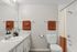 Modern bathroom with sleek granite countertop, stylish white cabinetry, and vibrant rust-colored towels providing a chic, welcoming atmosphere.