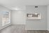 Bright apartment interior featuring a large window, modern wood flooring, and a cozy kitchen pass-through with dark cabinets.