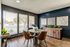 Chic dining area with a round table and leather chairs, large windows offering abundant natural light, and modern art pieces on a stylish dark accent wall.