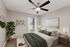 Elegant bedroom with modern decor, featuring a cozy bed with green linens, a stylish ceiling fan, and natural light streaming through a large window.