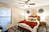 Charming bedroom with cozy decor, featuring a plush bed, vibrant orange accents, and stylish wall art, enhanced by warm lighting and a ceiling fan.
