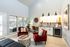 Bright and modern living area with elegant red armchairs, a stylish kitchenette, and large windows offering natural light and views of outdoor greenery.