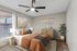 Elegant bedroom with modern decor, featuring a cozy bed with stylish cushions, a ceiling fan, and natural light streaming through large windows.