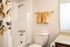Bright bathroom with elegant floral shower curtain, pristine white tiles, and modern fixtures. Complemented by soft gold towels, perfect for a relaxing retreat.