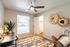 Charming bedroom with modern decor, featuring a cozy chair, colorful geometric rug, and stylish wall art under a sleek ceiling fan.