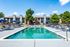 Inviting apartment complex with modern pool, sun loungers, and shaded seating, surrounded by lush greenery for a relaxing atmosphere.