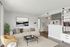Bright and modern living room featuring a stylish beige sectional sofa, elegant artwork, and sleek shelving, opening into a cozy dining area with contemporary decor.