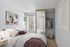 Cozy bedroom with modern decor, featuring a plush bed, stylish artwork, and a mirrored closet with hanging clothes, complemented by a green plant for a refreshing touch.