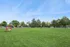 Expansive communal grassy area with a vibrant playground, surrounded by lush trees and with clear blue skies, offering a perfect space for outdoor activities.