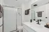 Modern bathroom featuring a sleek white sink, large mirror, and glass-enclosed shower, accented with black fixtures and fresh towels.