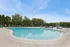 Inviting outdoor pool area with relaxing lounge chairs and lush greenery under a clear blue sky.