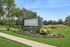 Scenic entrance to reNEW Poplar Creek surrounded by lush greenery and colorful landscaped flowers under a clear blue sky.