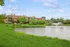 Charming apartment complex with stunning pond view and lush greenery, featuring a tranquil water fountain in a serene natural setting.