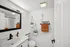 Bright and modern bathroom with stylish decor, featuring a sleek white countertop, elegant fixtures, and vibrant orange towels. Accentuated by hanging plants for a fresh touch.