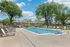 Inviting outdoor pool area with numerous lounge chairs, set against charming brick buildings and lush greenery under a bright blue sky.