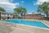 Inviting apartment complex with a sparkling outdoor pool, surrounded by sun loungers and shaded patio seating, set against a bright blue sky.