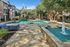 Luxurious apartment complex showcasing a sparkling pool, elegant stone pathways, lush greenery, and modern architecture.