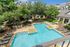 Luxurious apartment complex with a sparkling pool, shaded lounge areas, and lush greenery, perfect for relaxation and leisure.