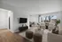 Inviting living room with modern decor, featuring plush seating, a chic coffee table, and a sleek wall-mounted TV, bathed in natural light from large windows.