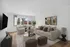 Bright living room with modern beige sofas, abstract wall art, and large windows offering natural light, featuring stylish decor and lush indoor plants.