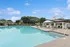 Inviting poolside retreat with elegant lounge chairs and umbrellas, surrounded by lush greenery and a charming clubhouse under a bright blue sky.