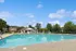 Inviting outdoor pool area with relaxing lounge chairs and lush greenery under a bright blue sky.