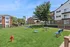 Vibrant community park with lush green lawn, picnic tables, and playground surrounded by modern apartment buildings.