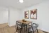 Modern dining area with a sleek wooden table, matching gray chairs, and contemporary artwork on a bright wall.