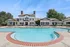 Elegant apartment complex featuring a sparkling swimming pool with poolside seating, surrounded by lush greenery and classic architecture.