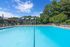 Luxurious apartment complex featuring a crystal-clear pool, surrounded by lush greenery and modern architecture under a vibrant blue sky.