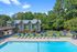 Inviting residential pool area with modern lounge chairs, surrounded by lush greenery and a clubhouse under clear blue skies.