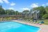 Charming apartment complex with a modern swimming pool, surrounded by lush greenery and comfortable poolside seating under a vibrant sky.