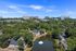 Stunning aerial view of a serene neighborhood surrounded by lush greenery and a tranquil pond with a fountain, set against a backdrop of modern city skyline.