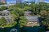 Captivating aerial view of serene apartments nestled in lush greenery, vibrant red doors, and a tranquil water feature, amidst a backdrop of modern urban towers.
