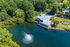 Scenic aerial view of a lakeside clubhouse with a vibrant fountain and rainbow, surrounded by lush greenery and featuring a large swimming pool.