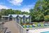 Charming clubhouse with a spacious deck overlooking lush greenery and a stylish poolside lounging area with blue chairs, providing a perfect retreat in a serene setting.